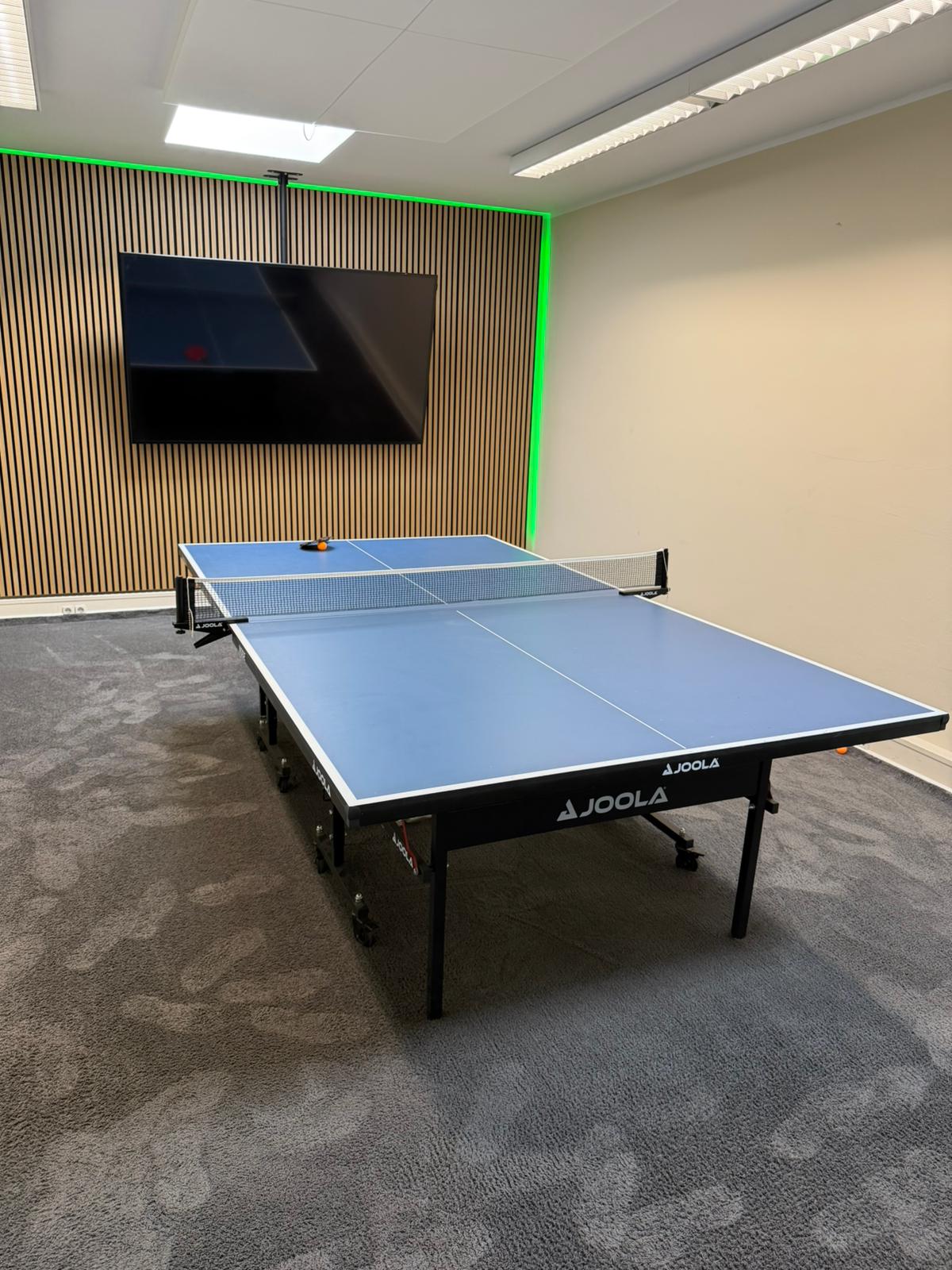 Die Creative Break & Energy Zone mit einer Joola-Tischtennisplatte und einem Monitor an der Holzlamellenwand für aktive Team-Momente