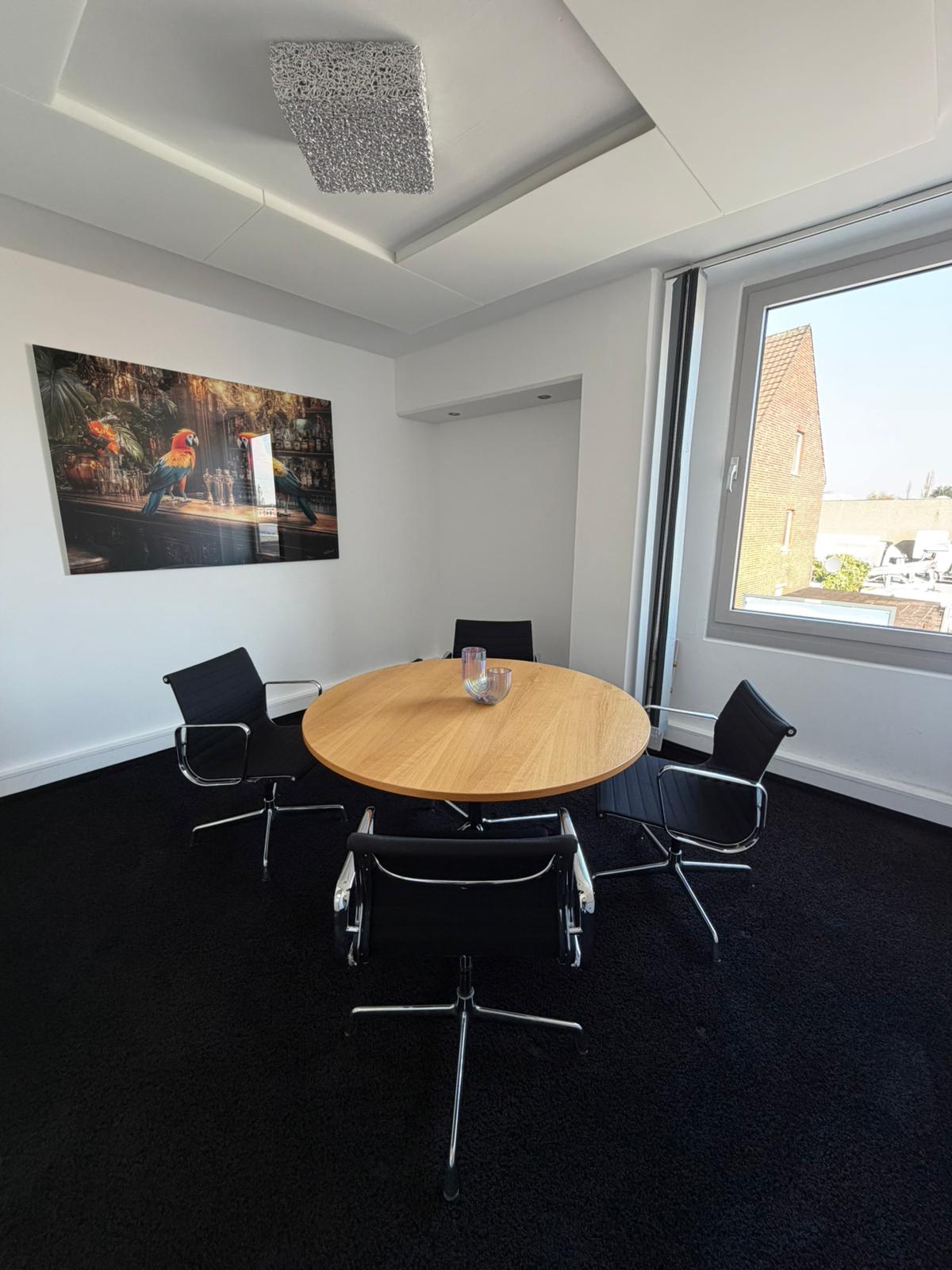 Ein heller, kleiner Besprechungsraum mit einem runden Holztisch und vier schwarzen Design-Stühlen