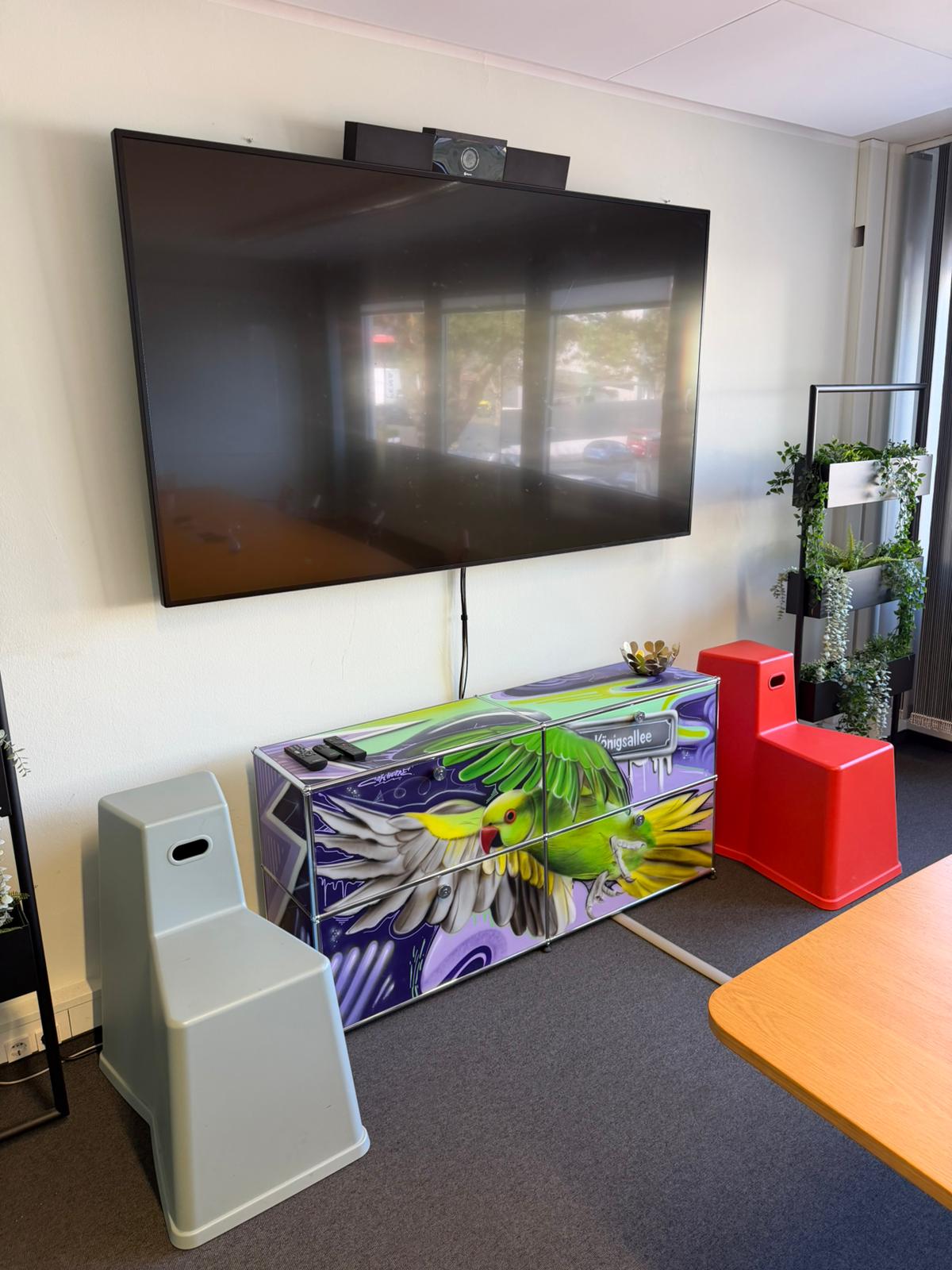 Ein Detail im Executive Meeting Space: Ein mit Graffiti verzierter USM-Schrank unter einem Monitor mit Trittsteinhockern